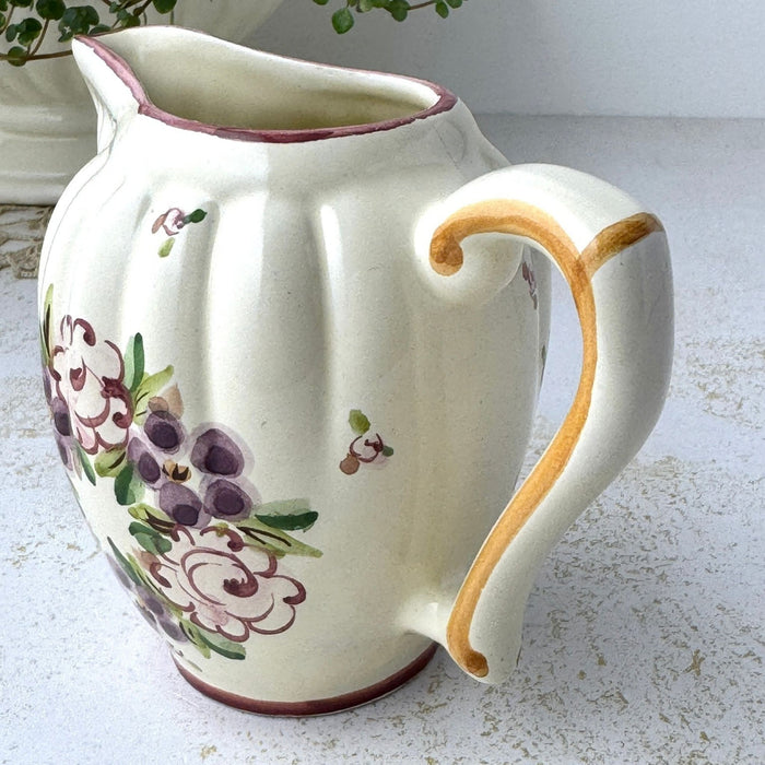 Close-up of creamer showing golden brown painted handle, cream glaze, and part of the floral decoration.