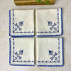Matching embroidered napkins folded together, showing their off-white woven fabric, blue embroidery and coordinating crocheted edges.