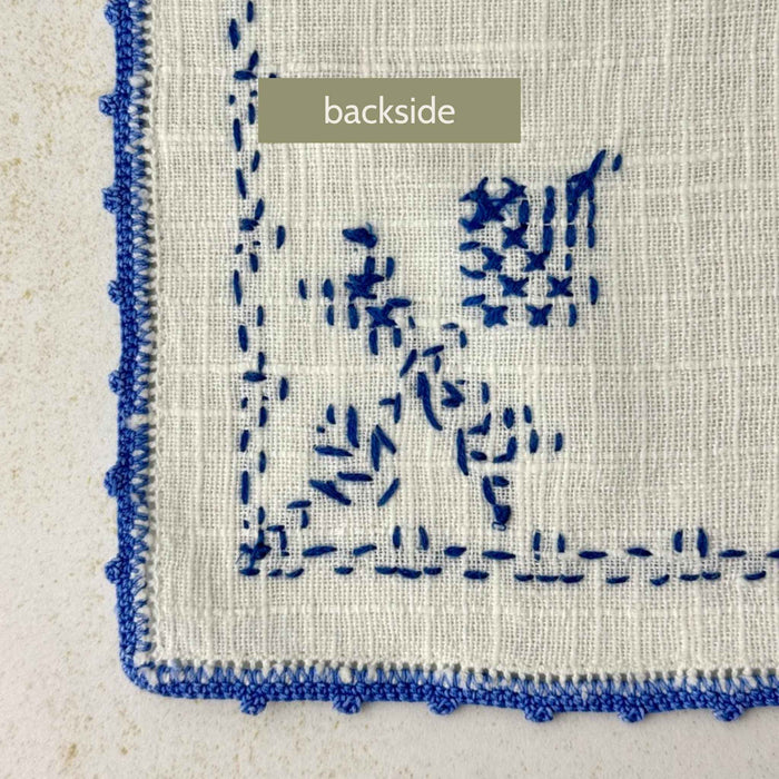 Reverse side of the embroidered napkin showing the back of the blue cross-stitch work and the woven fabric.