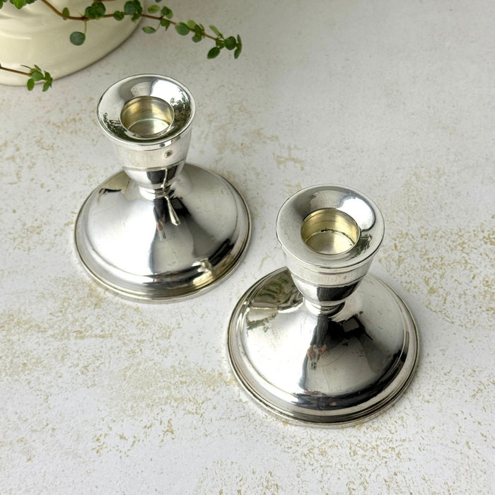 Pair of polished sterling silver Duchin candlesticks with wide circular bases and cup-shaped candle sockets, photographed from above on a light stone-textured surface.