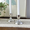 Pair of Duchin sterling silver candlesticks holding white taper candles, styled on a crocheted table runner in front of framed botanical artwork.