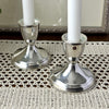 Close-up of two polished sterling silver candlesticks with white taper candles, showing their gently tapered stems, rounded bases, and reflective surfaces.