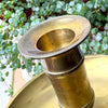 Close-up of the flared candle cup and cylindrical stem of an aged brass chamberstick, showing the warm, uneven patina.