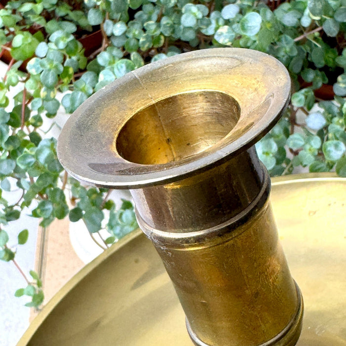 Close-up of the flared candle cup and cylindrical stem of an aged brass chamberstick, showing the warm, uneven patina.