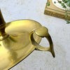 Close-up of the brass chamberstick's open finger loop handle attached to the rim of the circular drip pan.