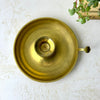 Overhead view of a brass chamberstick showing its wide circular drip pan, central candle cup, and side handle.