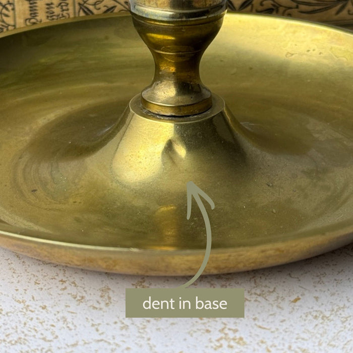 Close-up of the brass chamberstick base with an arrow identifying a small dent near the central stem.