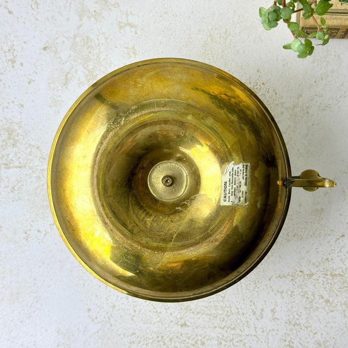 Underside of the brass chamberstick showing its circular construction and surviving paper safety label.