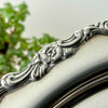 Close-up of the silverplate tray's raised border showing a five-petal flower, leaves, and curved scrolling details.