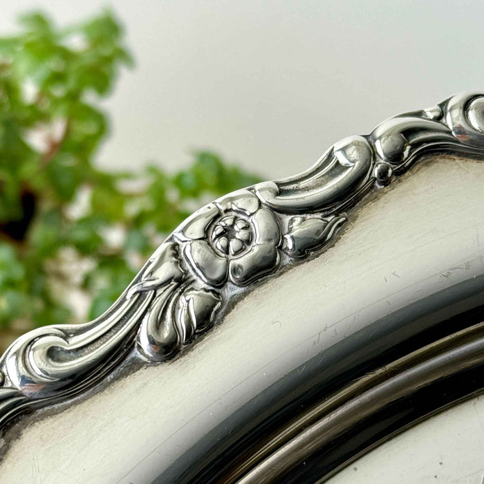 Close-up of the silverplate tray's raised border showing a five-petal flower, leaves, and curved scrolling details.
