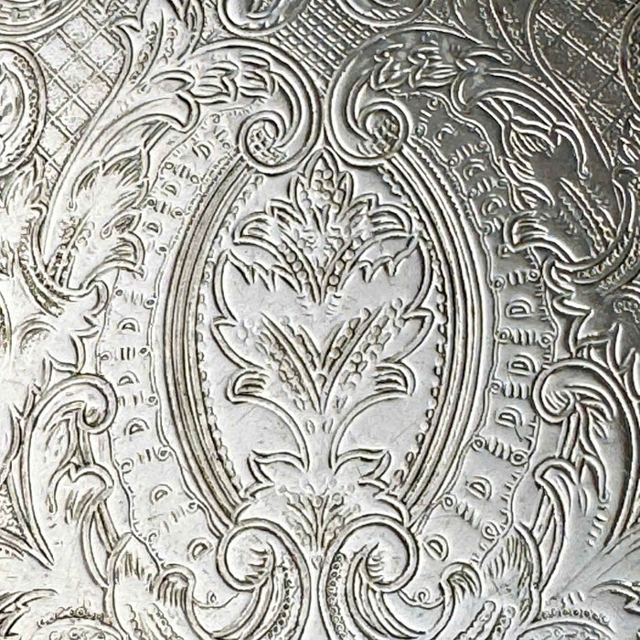 Close-up of the tray's embossed decoration showing an oval floral motif surrounded by elaborate scrollwork and textured details.