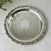 Round silverplate serving tray with an ornate scalloped floral border and intricate scrolling decoration across the center, photographed from above.