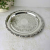 Round silverplate tray photographed at an angle, showing its wide raised rim, scalloped floral border, and decorated center.