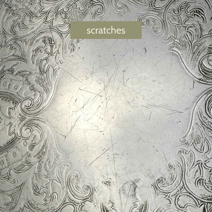 Close-up of the tray's center showing numerous fine scratches across the plain silverplate surface between the decorative motifs.