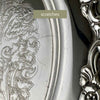 Close-up of the tray's outer surface showing scratches beside the embossed decoration and raised floral border.