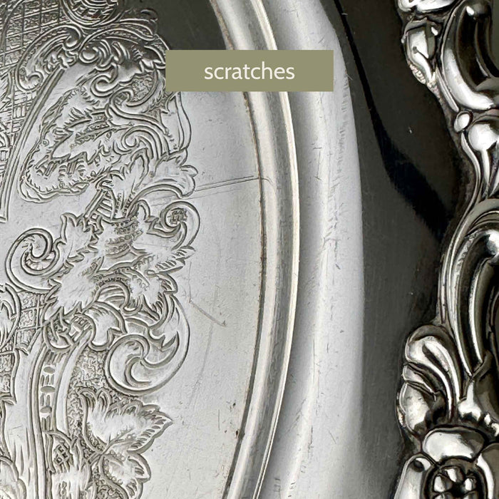 Close-up of the tray's outer surface showing scratches beside the embossed decoration and raised floral border.