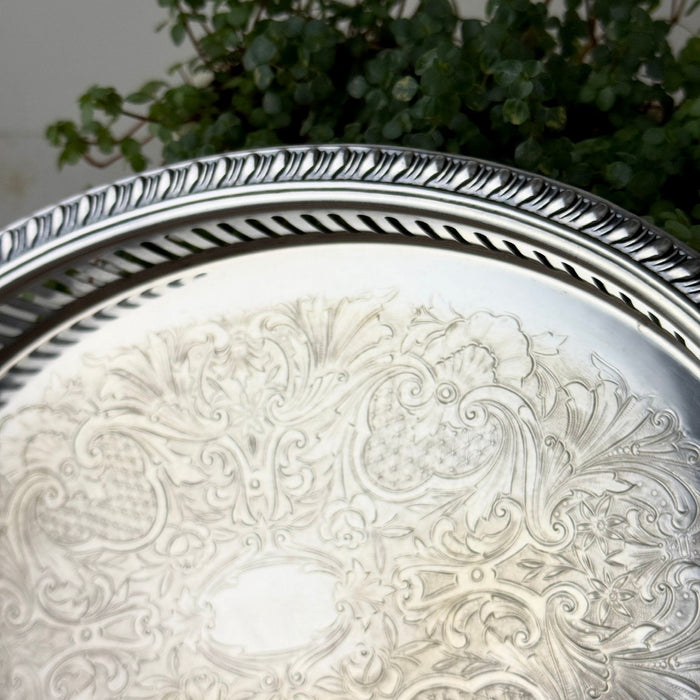 Close-up of the tray's rolled decorative rim, pierced vertical gallery openings, and finely detailed floral scrollwork on the silver surface.