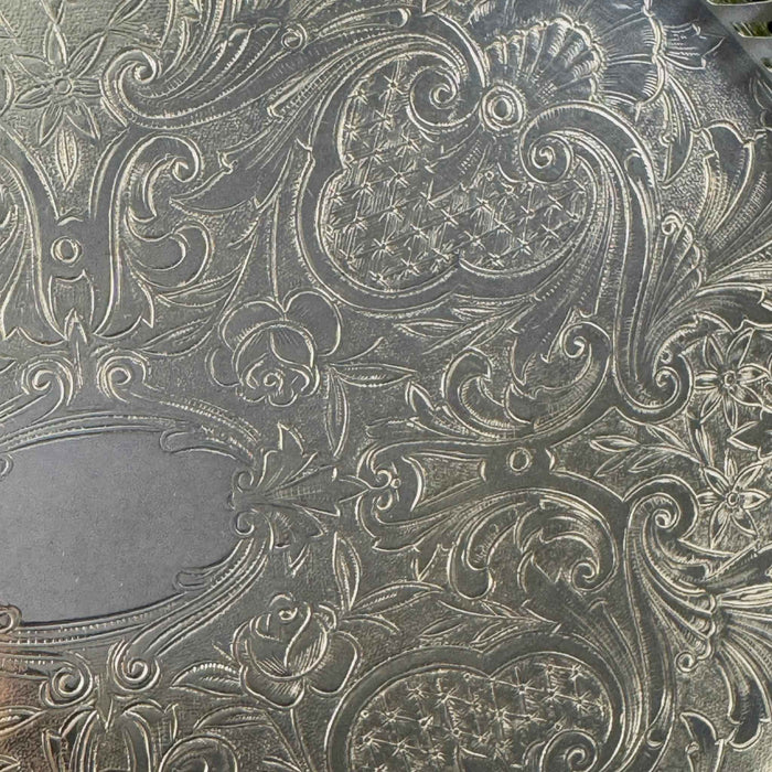 Close-up of embossed roses, curling leaves, crosshatched textures, and ornamental scrolls decorating the tray's base.