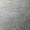 Detailed view of the central oval cartouche surrounded by embossed roses, foliage, scrollwork, and textured patterns.