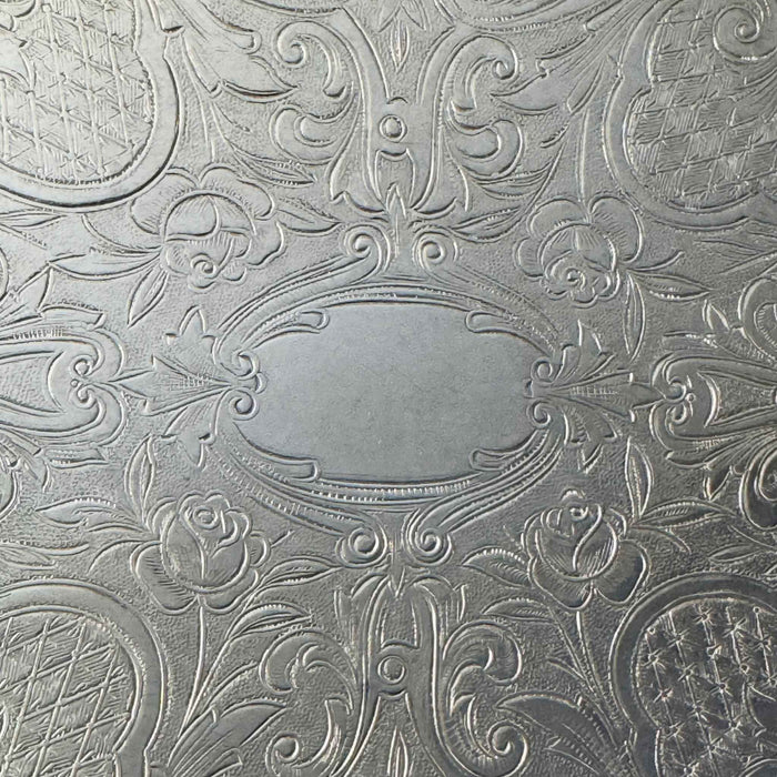 Detailed view of the central oval cartouche surrounded by embossed roses, foliage, scrollwork, and textured patterns.