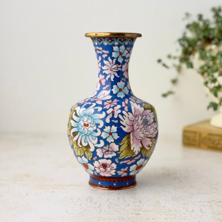 Vintage Chinese cloisonné vase with a rounded body, narrow flared neck, and mid-blue ground covered in pink, pale blue, and white flowers with green leaves and brass trim.