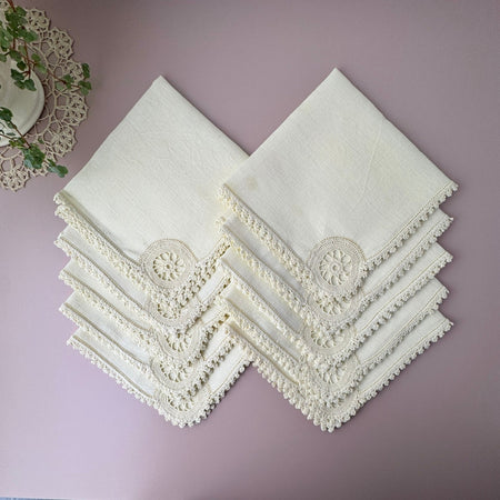 Set of ten vintage cream cloth napkins arranged in overlapping folds, showing matching crocheted edging and circular crochet medallions at the corners.