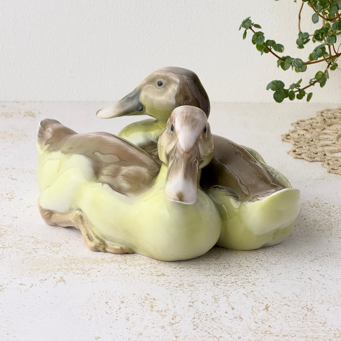 Front view of the porcelain duck pair, showing one duck facing forward and the other looking to the left, with brown wings and pale yellow-green bodies.