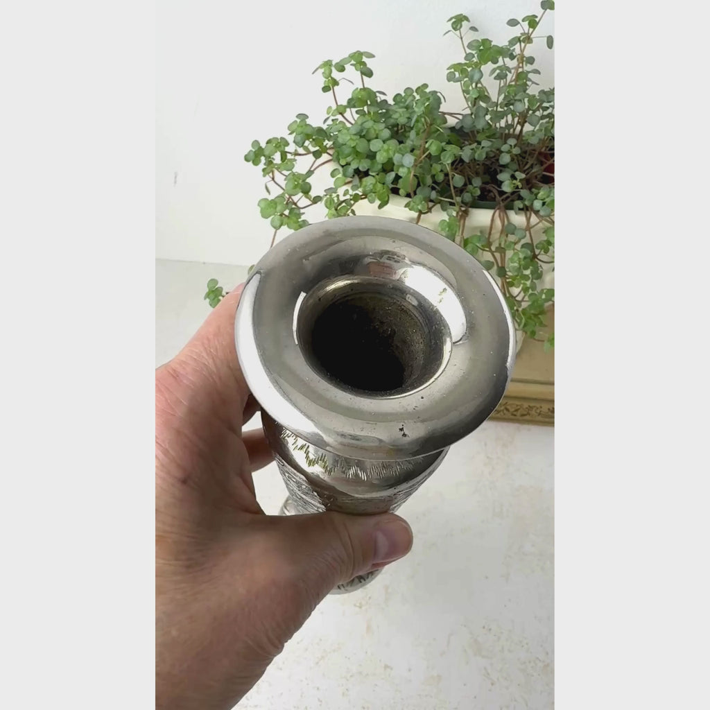 Vintage silver-colored brass bud vase rotated by hand to show the engraved floral decoration, narrow flared neck, and round footed base.