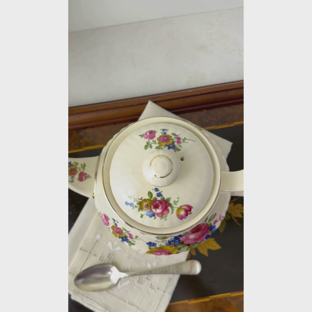 Vintage Sadler England teapot shown from  above and then in profile from spout to handle displaying the pink, blue, and golden-brown floral bouquets, ribbed cream ceramic body, and gold trim.