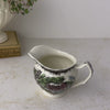 Vintage Johnson Bros Friendly Village creamer shown on a neutral backdrop, picked up and rotated to show its surface and interior