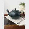 Matte black Pristine England teapot in a styled setting, shown from the front, spout side, overhead, and handle side