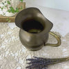Close view of a vintage brass pitcher with aged patina, panning from the open rim and interior down to reveal the rounded body, curved handle, and full profile