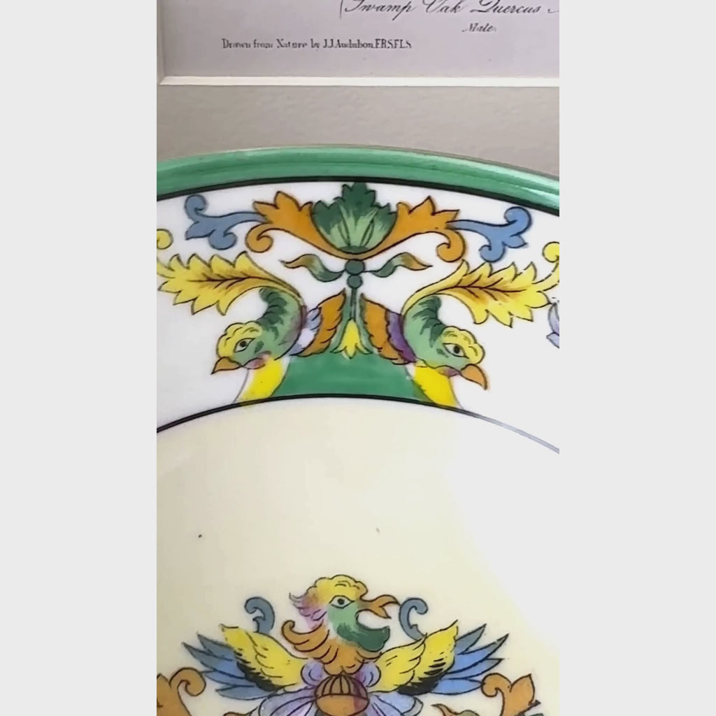 Close-up video of small cream-colored porcelain bowl with a green rim and colorful bird and floral decoration inside.