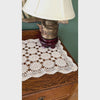Video of ecru crochet table runner styled across a dark wood table with brass candlesticks, white candles, and a white planter with greenery.