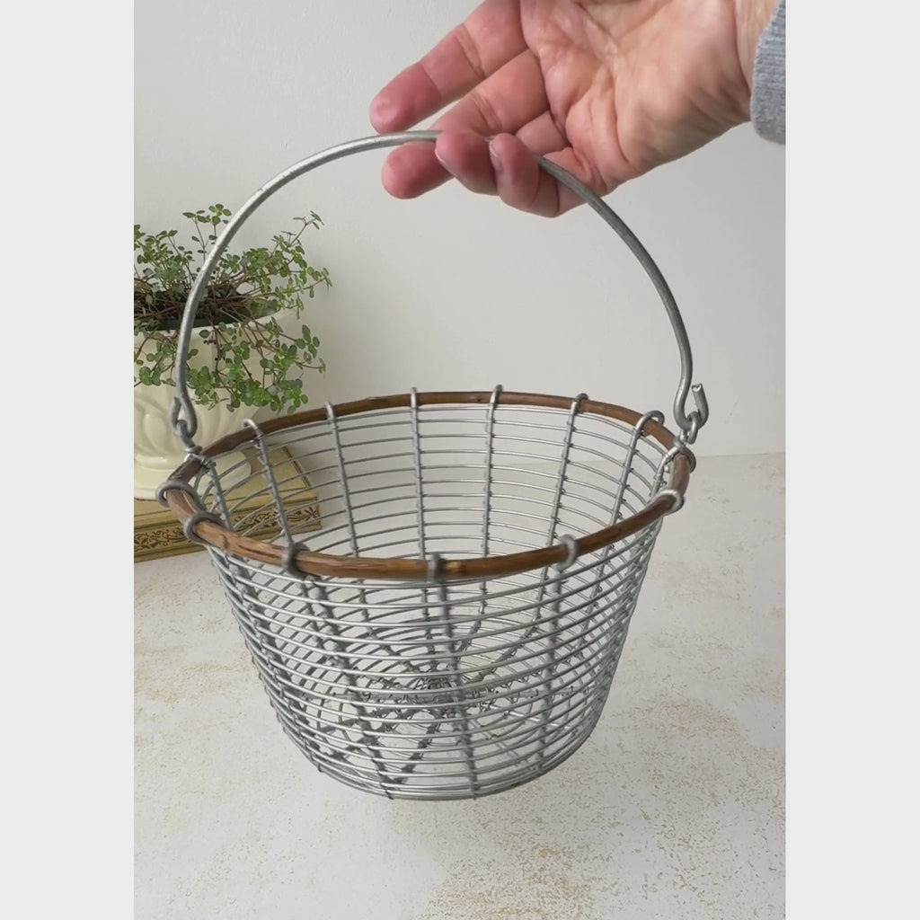 Vintage wire egg gathering basket shown on a neutral backdrop as it is rotated by the handle to show front and back and then the basket handle is lowered
