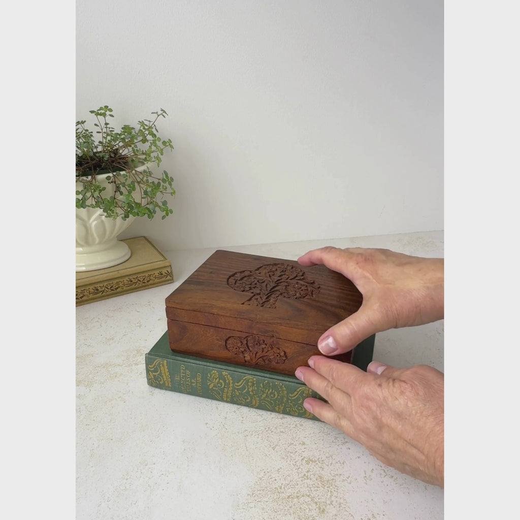 Vintage hand-carved wood keepsake box is opened and tilted to show the purple felt lined interior with light contrasting trim