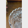 Closeup video of a round clear glass dish with three radiating flowers, pointed leaves, geometric star patterns, and a deeply notched rim.