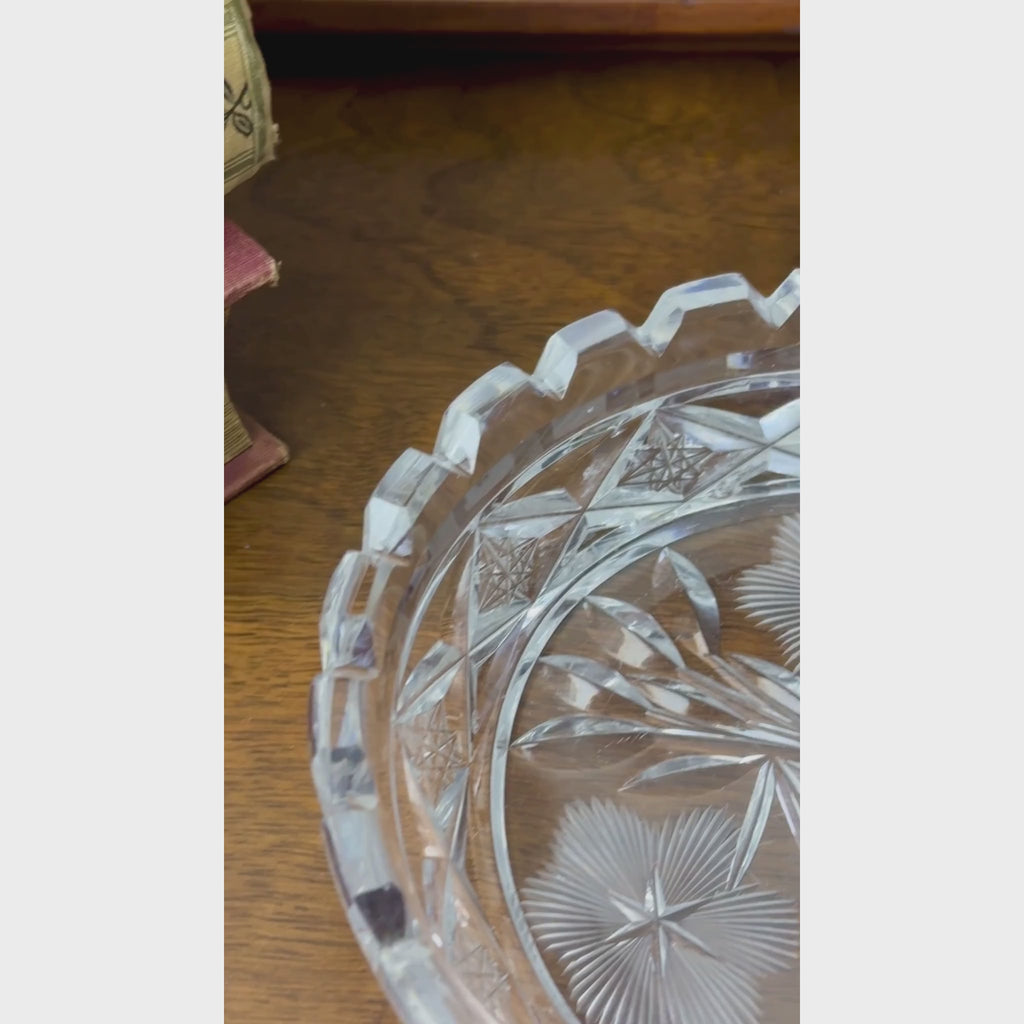 Closeup video of a round clear glass dish with three radiating flowers, pointed leaves, geometric star patterns, and a deeply notched rim.