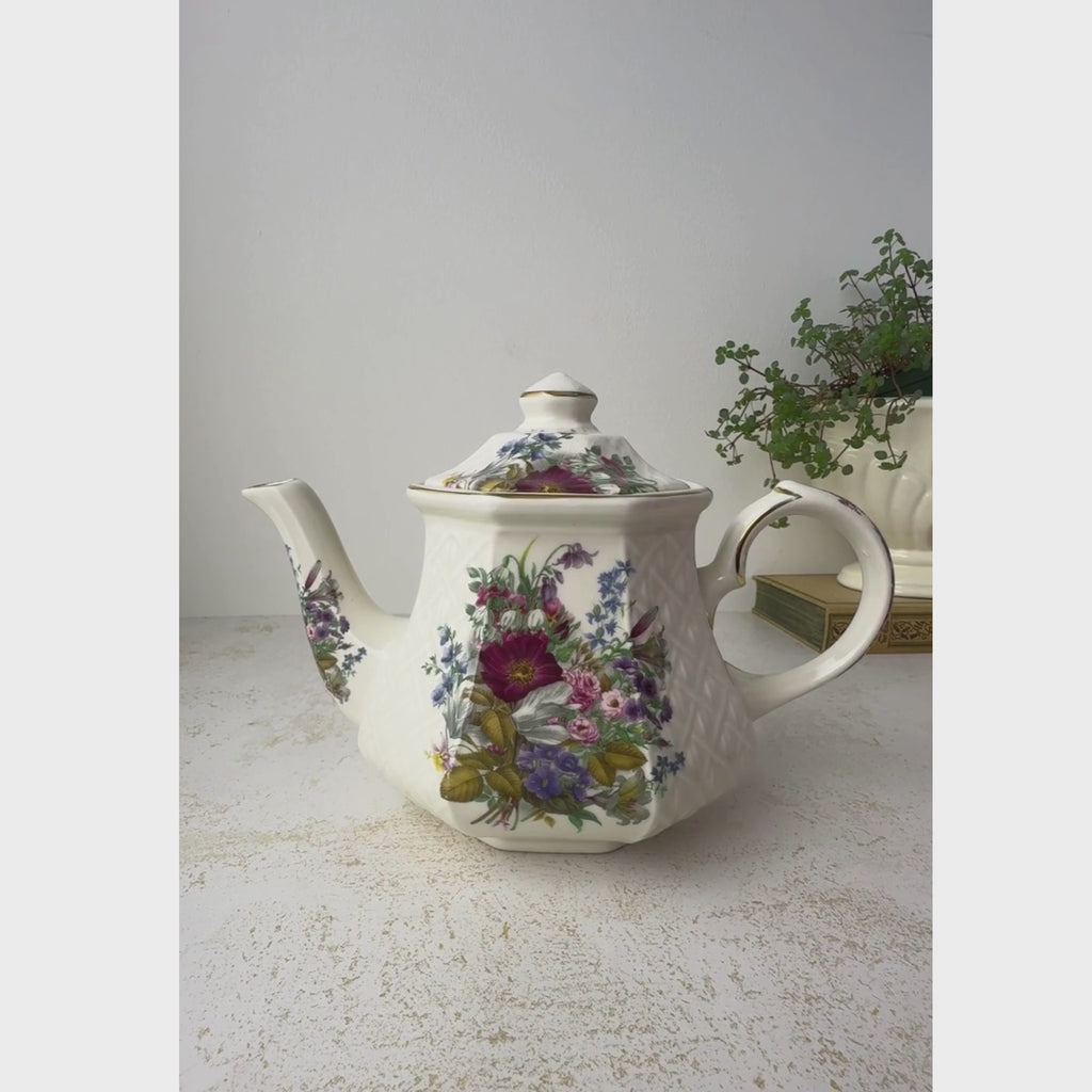 Vintage Sadler Windsor teapot with multicolor floral decoration, embossed basket-weave sides, and gold trim styled with trailing plant with the lift and pour action being demonstrated
