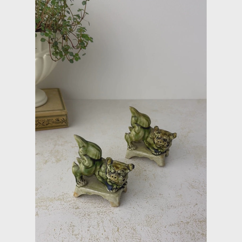 Pair of vintage foo dog figurines shown teogether on a neutral backdrop, then the back figurine is handled to show the shape and underside