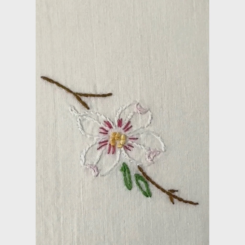 Close-up pan of embroidered dogwood blossoms and scalloped crochet edging on vintage pillowcase