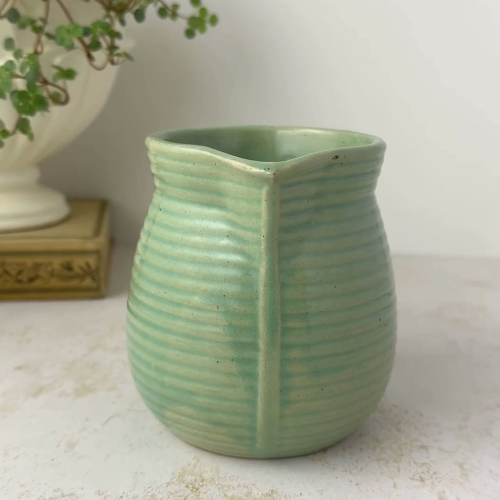 Small vintage Monmouth Pottery stoneware pitcher with ribbed body and soft green glaze rotated from spout facing to side view