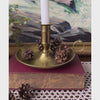 Video of vintage brass chamberstick holding a white taper candle, styled with pinecones on a burgundy book.