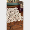 Video of ecru crochet table runner displayed on dark wood sideboard, showing repeating floral rosettes, openwork pattern, looped details, and scalloped edge.