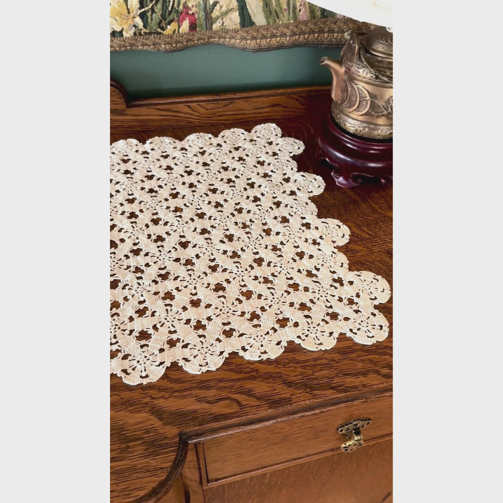 Video of ecru crochet table runner displayed on dark wood sideboard, showing repeating floral rosettes, openwork pattern, looped details, and scalloped edge.