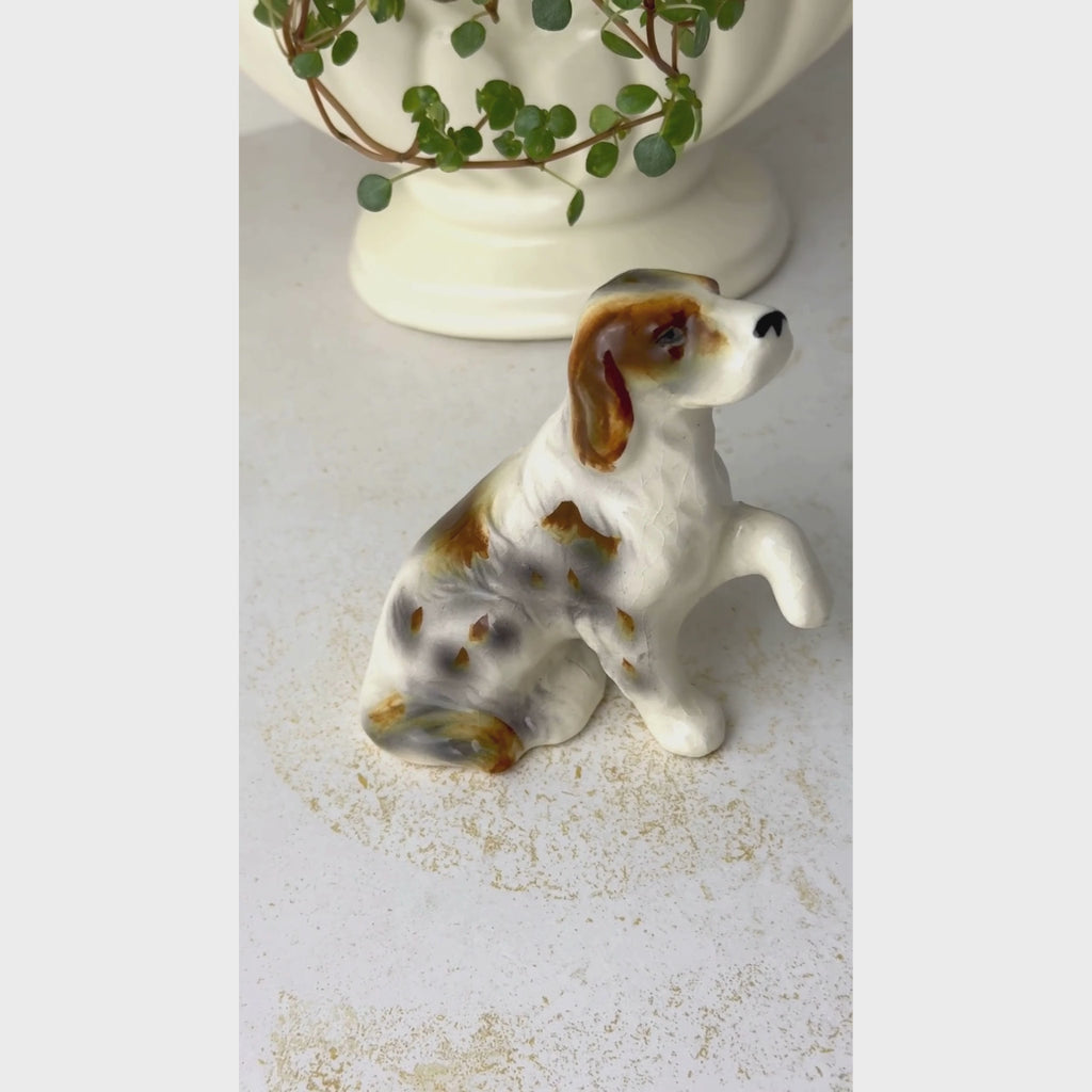 Video of small hand-painted ceramic dog figurine with a raised front paw, brown and gray markings.