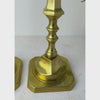 Tall brass candlestick shown close-up from the square base up the long decorative stem to the hexagonal candle cup