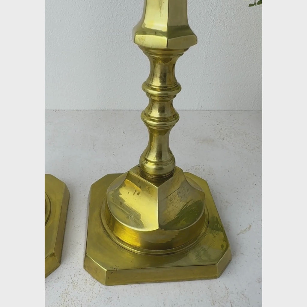 Tall brass candlestick shown close-up from the square base up the long decorative stem to the hexagonal candle cup