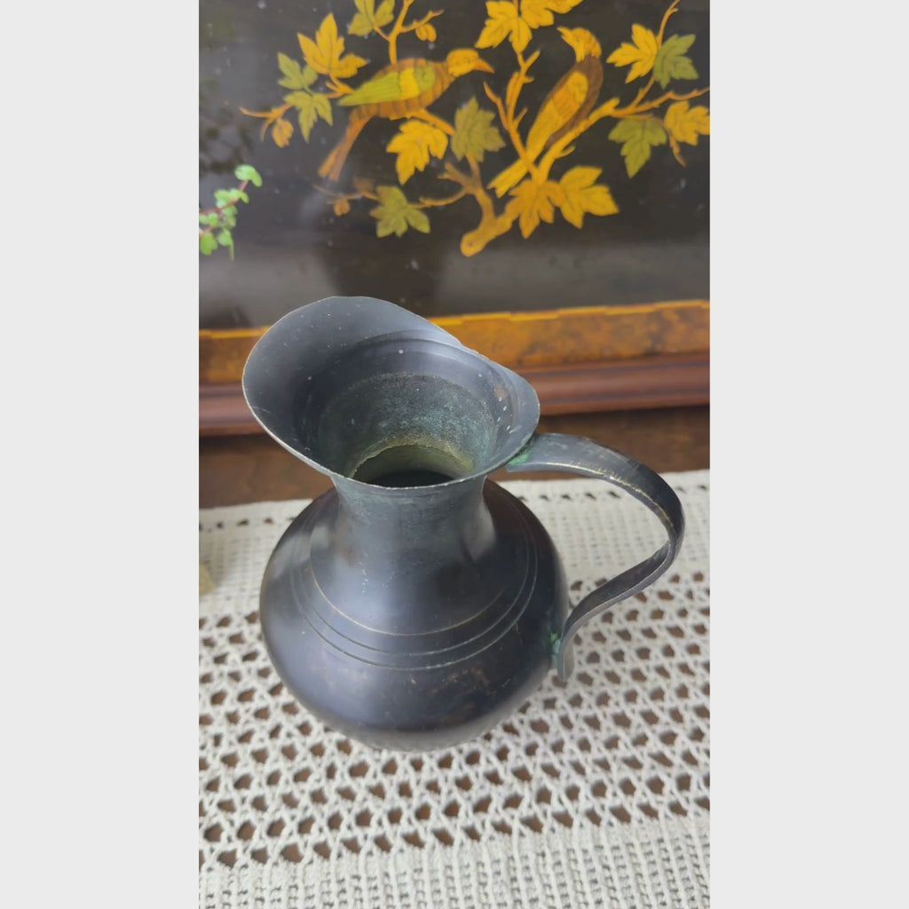 Video showing top and sides of a small vintage blackened brass pitcher in front of a decorative inlaid tray.