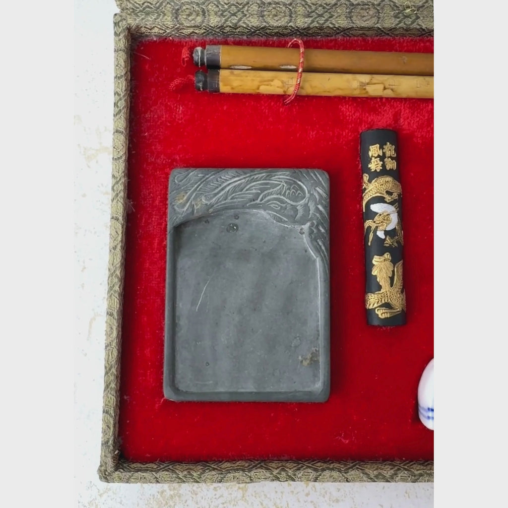 Open vintage Chinese calligraphy set in a fitted textile-covered box with red lining shown close-up starting with the brushes, inkstone and ink on the left to the carved seal, brass spoon, and porcelain tools on the right
